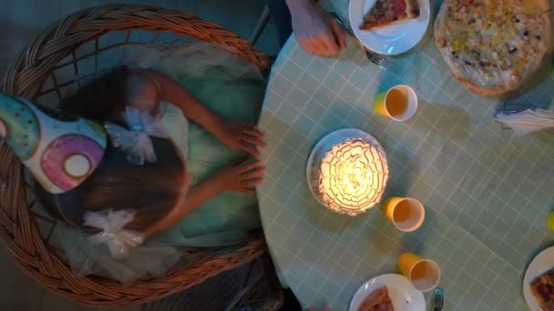 家族と親のクリエイティブなコンセプト リビングのシーン パーティーフード付きのテーブルのトップビュー クローズアップガールはケーキにろうそくを吹く 家族や友人は小さな女の子の誕生日を祝う — ストック動画