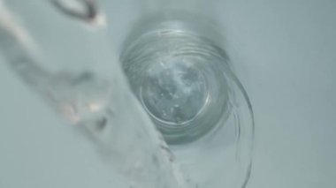 Çerçevede beyaz bir masanın üzerinde cam bir cam var. Sonra içine su dökmeye başlıyorlar. Kamera yavaşça yaklaştı ve battı, kabarcıklar ve maden suyu damlalarını gösterdi. Makro fotoğraf.