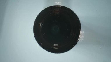 Çerçevede beyaz bir masanın üzerinde bir cam var. Sonra içine dökülmeye başlıyorlar. Kamera yavaşça yaklaştı ve battı, kabarcıklar ve maden suyu damlalarını gösterdi. Makro fotoğraf.