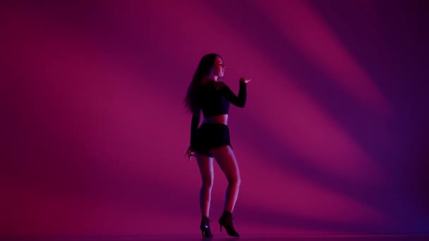 スタジオで踊る魅力的な女性 ピンクとブルーネオンライト 影の背景 ブラックセクシーな衣装 ハイヒール 現代の振付 全長について プロモーションクリップや広告 — ストック動画