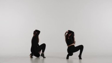 Stüdyoda dans eden iki kadın. Düz beyaz izole arka plan. Siyah seksi kostüm, yüksek topuklu ayakkabı. Modern şehvetli koreografi. Tam boy. Reklam videosu veya reklamı.