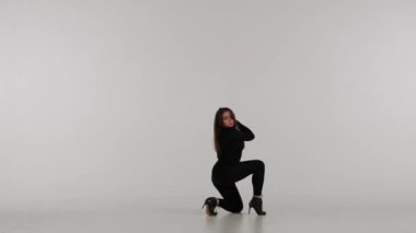 Stüdyoda dans eden çekici kadın. Düz beyaz izole arka plan. Siyah seksi kostüm, yüksek topuklu ayakkabı. Modern şehvetli koreografi. Tam boy. Reklam videosu veya reklamı.