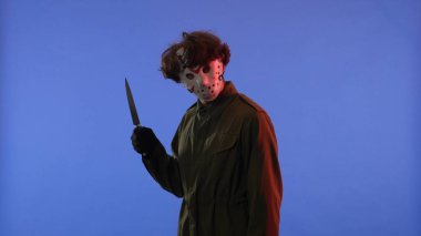 Beyaz maskeli, elinde keskin bir bıçakla mavi arka planda kırmızı ışıklı bir adam. 13. Cuma 'dan manyak Jason Voorhees' in resmi. Cadılar Bayramı konsepti.