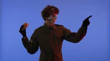 Elinde hamburgerle beyaz maskeli bir adam mavi arka planda kırmızı ışıklı parmağını işaret ediyor. 13. Cuma 'dan manyak Jason Voorhees' in resmi. Cadılar Bayramı konsepti