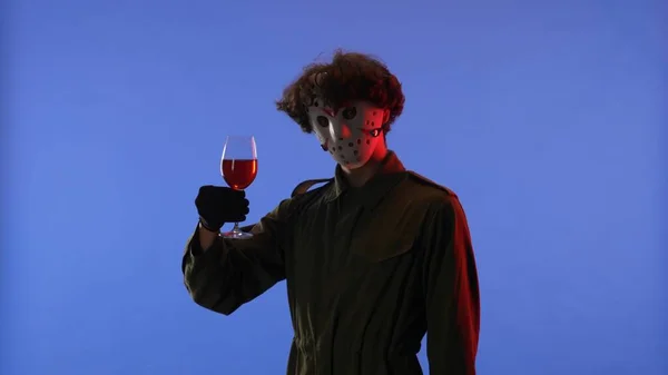 戴白面罩的男人拿着一杯红葡萄酒 蓝色背景 红色霓虹灯 狂人Jason Voorhees的照片来自13号星期五万圣节庆祝概念 — 图库照片