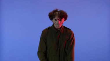 Beyaz maskeli, elinde testereyle mavi arka planda kırmızı ışıklı bir adam. 13. Cuma 'daki Jason Voorhees manyağı. Cadılar Bayramı konsepti.