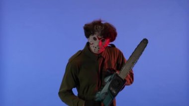 Beyaz maskeli, elinde testereyle mavi arka planda kırmızı ışıklı bir adam. 13. Cuma 'daki Jason Voorhees manyağı. Cadılar Bayramı konsepti.