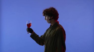 Beyaz maskeli bir adam kırmızı ışıklı, mavi arka planda kırmızı şaraplı bir bardak tutuyor. 13. Cuma 'dan manyak Jason Voorhees' in resmi. Yan görüş. Cadılar Bayramı konsepti