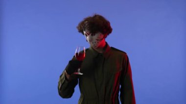 Beyaz maskeli bir adam kırmızı ışıklı, mavi arka planda kırmızı şaraplı bir bardak tutuyor. 13. Cuma 'dan manyak Jason Voorhees' in resmi. Yan görüş. Cadılar Bayramı konsepti