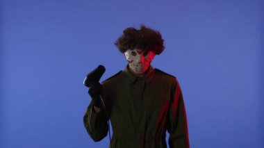 Beyaz maskeli, saçlarını kurutan, mavi arka planda saç kurutma makinesi olan, kırmızı ışıklı bir adam. 13. Cuma 'dan manyak Jason Voorhees' in resmi. Cadılar Bayramı konsepti