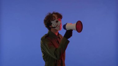 Beyaz maskeli, elinde hoparlörle mavi arka planda kırmızı ışıklı bir adam. 13. Cuma 'dan manyak Jason Voorhees' in resmi. Bir şey söylüyor. Cadılar Bayramı konsepti.