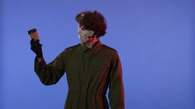 Beyaz maskeli ve bir fincan kahveli bir adam mavi arka planda kırmızı ışıklı bir jest gösteriyor. 13. Cuma 'daki Jason Voorhees manyağı. Cadılar Bayramı konsepti.
