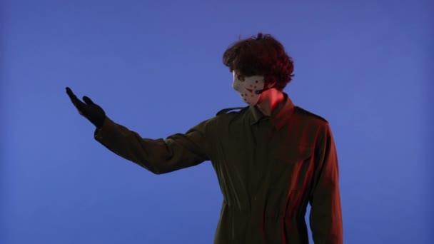 白いマスクの男は 赤いネオンライトで青い背景の方向に手を指しています 金曜日の13からのマニアックジェイソン ヴァイヘイズのイメージ ワークスペース ハロウィーンのお祝いのコンセプト — ストック動画