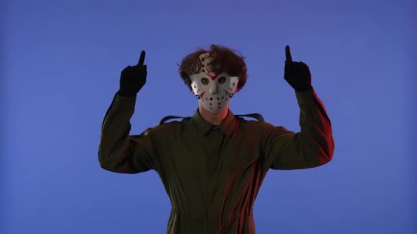 白いマスクの男は 赤いネオンライトで青い背景に指を向ける 13日の金曜日からジェイソン ヴァイエス マニアックのイメージ ワークスペース ハロウィーンのお祝いのコンセプト — ストック動画