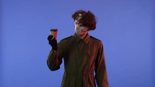 赤いネオンライトで青い背景にOkジェスチャーを示すコーヒーカップ付きの白いマスクの男 13日の金曜日からジェイソン ヴァイエス マニアックのイメージ ハロウィーンのお祝いのコンセプト — ストック動画