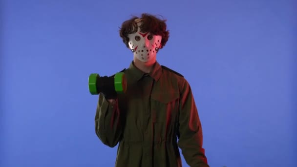 赤いネオンライトで青い背景に緑のダンベルで腕を振る白いマスクの男 金曜日の13からのマニアックジェイソン ヴァイヘイズのイメージ ハロウィーンのお祝いのコンセプト — ストック動画