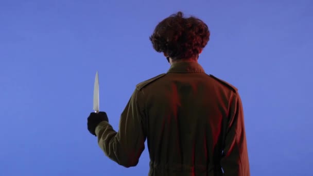 赤いネオン ライトが付いている青い背景の大きい鋭いナイフを持つ男 13日の金曜日からジェイソン ヴァイエス マニアックのイメージ バックビュー ハロウィーンのお祝いのコンセプト — ストック動画