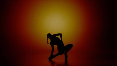 Modern dans stili yaratıcı reklam konsepti. Kadın dansçı portresi. Yüksek topuklu kadın dansçı silueti koyu sarı spot ışıklarıyla kameraya poz veriyor. Renkli arkaplanda izole.