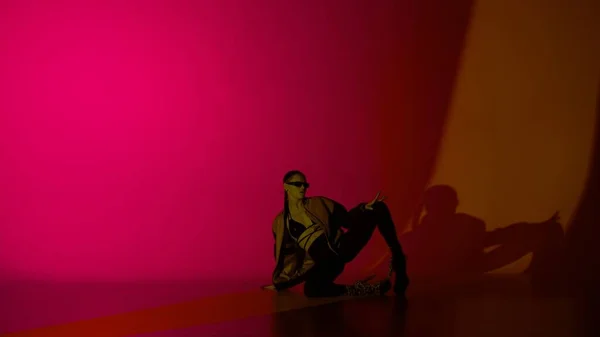現代ダンススタイルのクリエイティブ広告コンセプト 女性ダンサーの肖像画 ピンクのネオンライトのスタジオで床に座っている高ヒールの女性ダンサー 鮮やかなカラフルな背景に孤立した — ストック写真