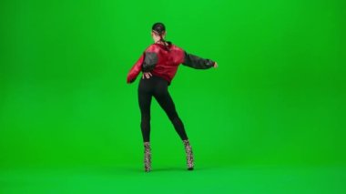 Modern koreografi ve dans stili yaratıcı konsept. Ceketli çekici bir kadın, yüksek topuklu ayakkabılarla stüdyoda yeşil ekran arka planda dinamik ve şehvetli dans ediyor. Reklam alanı modeli.