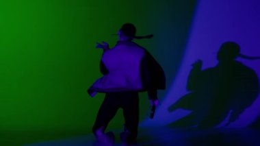 Modern koreografi ve dans yaratıcı konsepti. Kadın dansçı portresi. Gözlüklü ve topuklu ayakkabılarla dans eden çekici kadın stüdyoda yerde mavi yeşil ışıklı arka planda..