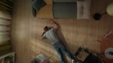 Tekerlekli sandalyeden düştükten sonra engelli bir adam oturma odasında yerde yatıyor. Kanepeye emeklemeye çalışan bir adamın en iyi görüntüsü. Adam çaresizlikten yumruklarını yere vuruyor.