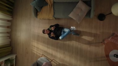 Oturma odasının zemininde elinde akıllı bir telefonla yatan bir adamın en üst görüntüsü. Adam online bir oyun oynuyor, kaybediyor, ellerini ve ayaklarını yere vuruyor, avuç içiyle yüzünü örtüyor.