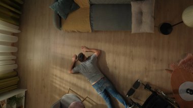 Tekerlekli sandalyeden düştükten sonra engelli bir adam oturma odasında yerde yatıyor. Çaresiz bir adamın yüzükoyun yere yatışı.