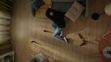 Oturma odasında sarhoş bir adamın etrafa saçılmış bira şişeleriyle çevrili görüntüsü. Adam kafası kanepede dinlenirken yerde oturarak uyuyor. Alkolizm. Umutsuzluk