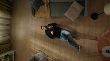 Oturma odasının zemininde elinde akıllı bir telefonla yatan bir adamın en üst görüntüsü. Şaşkın adam sosyal medyayı kontrol ediyor, fotoğraflara, videolara bakıyor. Aygıtlara bağımlılık