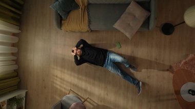 Şok olmuş bir adamın oturma odasının zemininde akıllı bir telefonun yanında yatışı. Adam orada başını tutarak yatıyor.