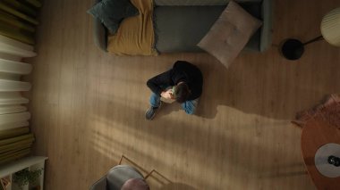 Oturma odasının zemininde, kanepenin yanında elinde akıllı bir telefonla oturan bir adamın en üst görüntüsü. Telefonda konuşan adam.