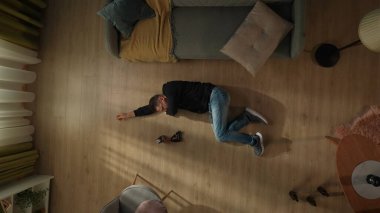 Alkolizm kavramı. Oturma odasının zemininde bir kül tablası ve bir şişe viskinin yanında yatan bir adamın en üst görüntüsü. Adam öksürürken eliyle ağzını kapatır.