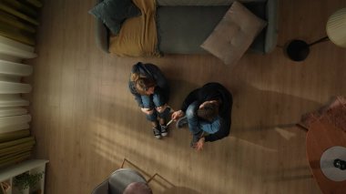 Oturma odasının zemininde kanepede oturan bir adamla bir kadının üst görüntüsü. Şok olmuş adam hamilelik testini pozitif tutuyor.