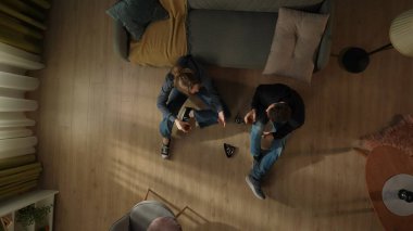 Oturma odasının zemininde oturan bir çiftin üst görüntüsü, aralarında bir şişe alkolle birlikte. Bardakları alkolle dolduran kadın ve erkek. Bir çift sorunlarından uzaklaşıyor.