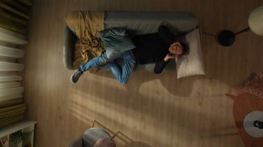 Oturma odasındaki kanepede yatan bir adamın en iyi görüntüsü. Adam şakaklarını ovuyor, şiddetli baş ağrısı, migren. Migren, baş ağrısı, stres, gerilim sorunu, akşamdan kalma konsepti