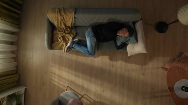 Oturma odasındaki kanepede yatan bir adamın en iyi görüntüsü. Adam şakaklarını ovuyor, şiddetli baş ağrısı, migren. Migren, baş ağrısı, stres, gerilim sorunu, akşamdan kalma konsepti