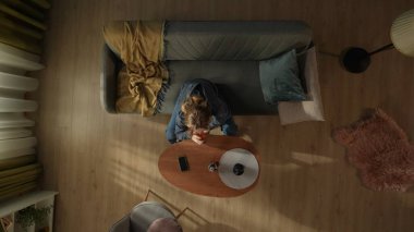 Oturma odasındaki kanepede oturan bir kadının kahve masasının önünde elinde bir şişe alkolle görüntüsü. Kadın telefon ya da mesajını beklerken alkol alıyormuş.