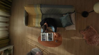 Oturma odasındaki kanepede oturan bir adamın bir şişe alkol ve bardakla kahve masasının önünde görüntüsü. Adam fotoğraf albümüne bakıyor. Boşanma, ayrılma.