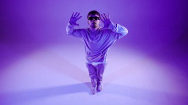 Mor arka planda duran bir adam var. Kamera hafifçe tepemizde. Dans hareketini gösteriyor, ışık huzmeleri onun üzerinde parlıyor. Sokak tarzı giyinmiş olarak. Plastik, ritmik..