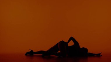 Kırmızı, turuncu arkaplanda. Açık giysileri ve yüksek topuklu ayakkabıları olan siluetli bir kadın. Dans hareketini gösteriyor, poz veriyor. Kalçası yukarda yerde yatıyordu. Seksi, plastik oynuyor.