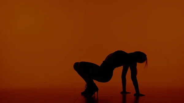 在一个红色 橙色的背景上的框架 一个穿着轮廓的女人穿着敞开的衣服和高跟鞋 展示舞蹈动作和姿势 她双手放在地板上坐下 她很性感 — 图库照片