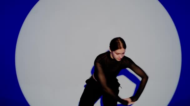 现代编舞和舞蹈风格的创意理念 女舞蹈家的画像 穿着黑色服装的迷人女孩在工作室的蓝色背景聚光灯下跳着现代现代舞 近距离拍摄 — 图库视频影像