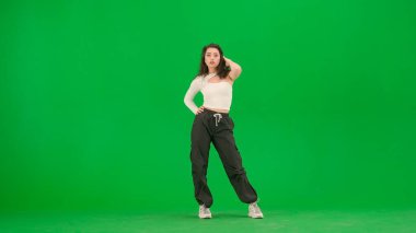 Modern dans koreografisi yaratıcı reklam konsepti. Beyaz bluzlu ve siyah pantolonlu çekici bir kadın caz funk dansında poz veriyor krom anahtar yeşil ekran arka planında kameraya bakıyor..