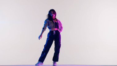 Modern dans koreografisi yaratıcı reklam konsepti. Beyaz bluzlu, siyah pantolonlu, kırmızı-mavi ışıklı caz funk dansı yapan, stüdyoda beyaz arka planda izole edilmiş çekici bir kadın..