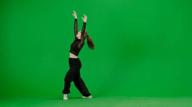 Modern yaratıcı koreografi ve dans konsepti. Kadın dansçı portresi. Siyah elbiseli çekici genç kız krom anahtar yeşil ekran arka planında modern dans ediyor..