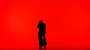 Modern yaratıcı koreografi ve dans konsepti. Kadın dansçı portresi. Siyah kıyafetli çekici kız silueti stüdyodaki kırmızı arka planda modern dansın dans öğesini gösteriyor..