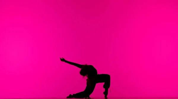 現代の創造的な振付とダンスのコンセプト 女性ダンサーの肖像画 スタジオでピンクのバックグラウンドでコンテンポラリーダンスを踊る床に黒い服で魅力的な少女のシルエット — ストック写真