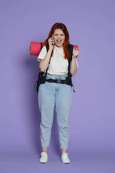 旅游和积极的业余时间广告概念 女旅行家的肖像穿着休闲装的女游客 背包里挂着智能手机 大喊大叫 被紫色背景隔离 — 图库照片
