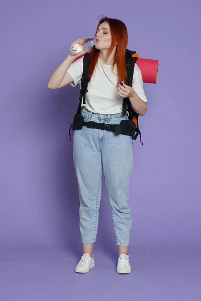旅游和积极的业余时间广告概念 女旅行家的肖像穿着休闲装的女游客 背包里拿着塑料瓶和饮用水 被紫色背景隔离 — 图库照片